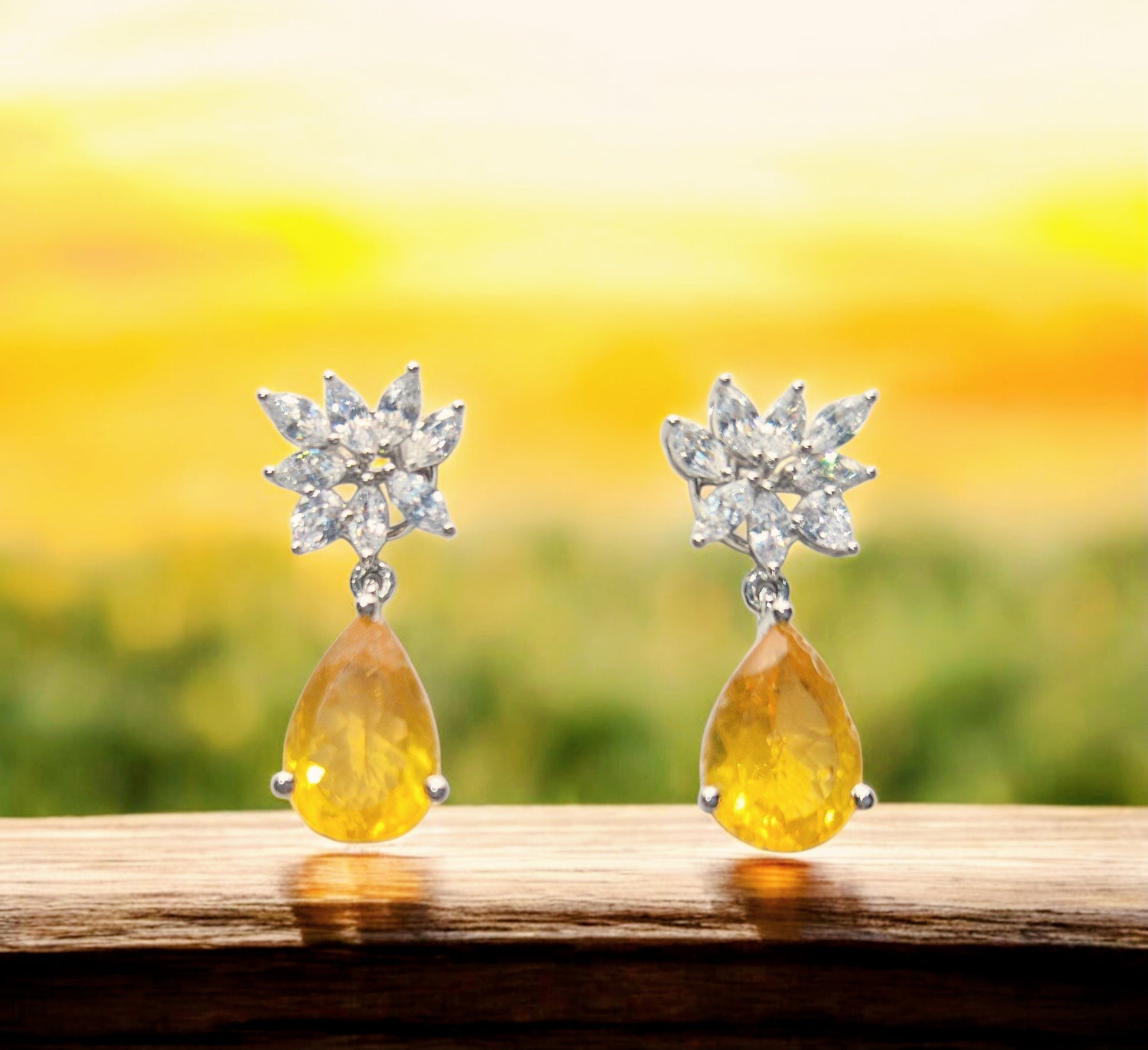 Pair of earrings with yellow teardrop stones and silver floral tops .